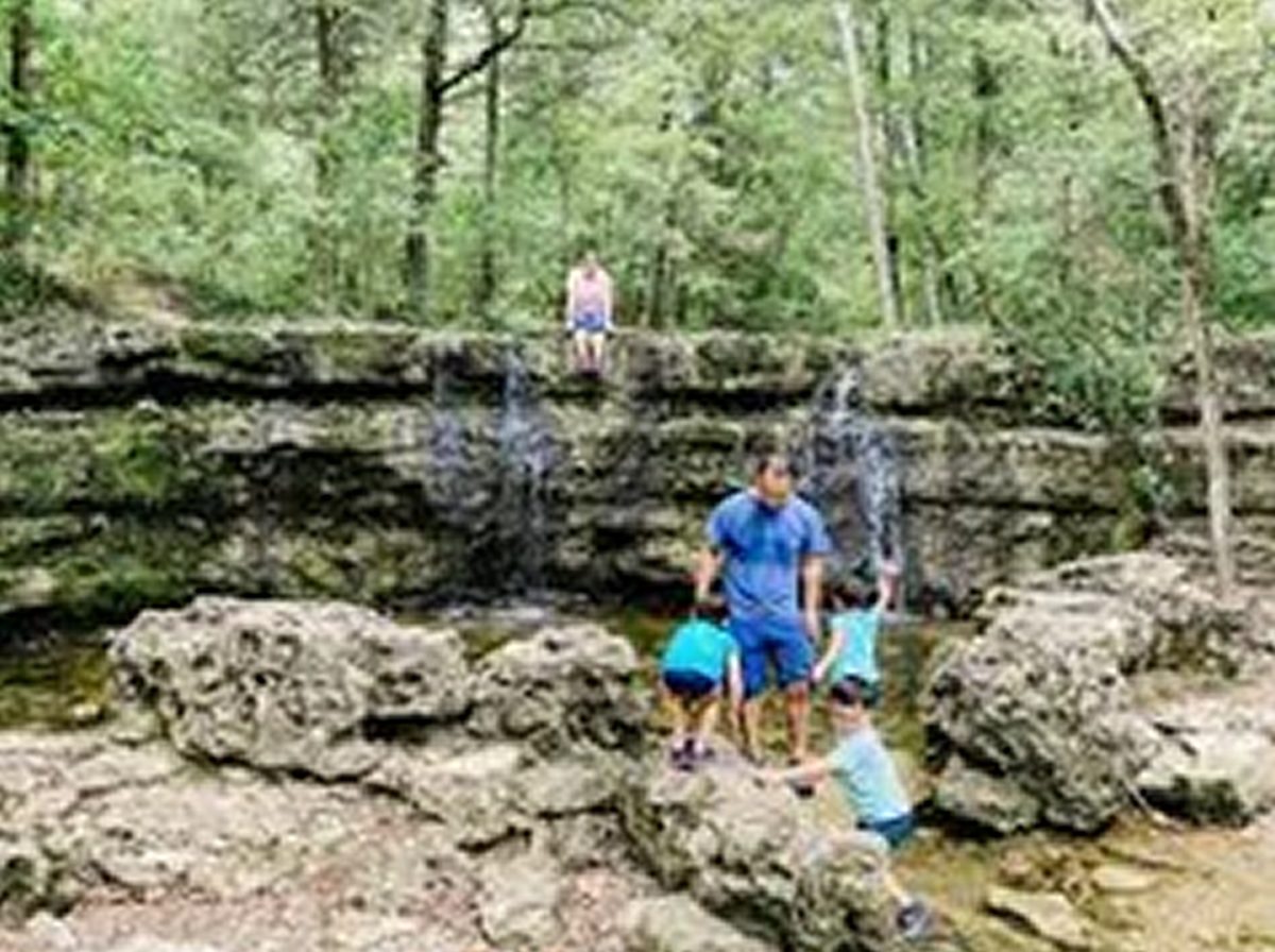 A family climbing the rocks below a small waterfall on an Ozarks trail near Branson